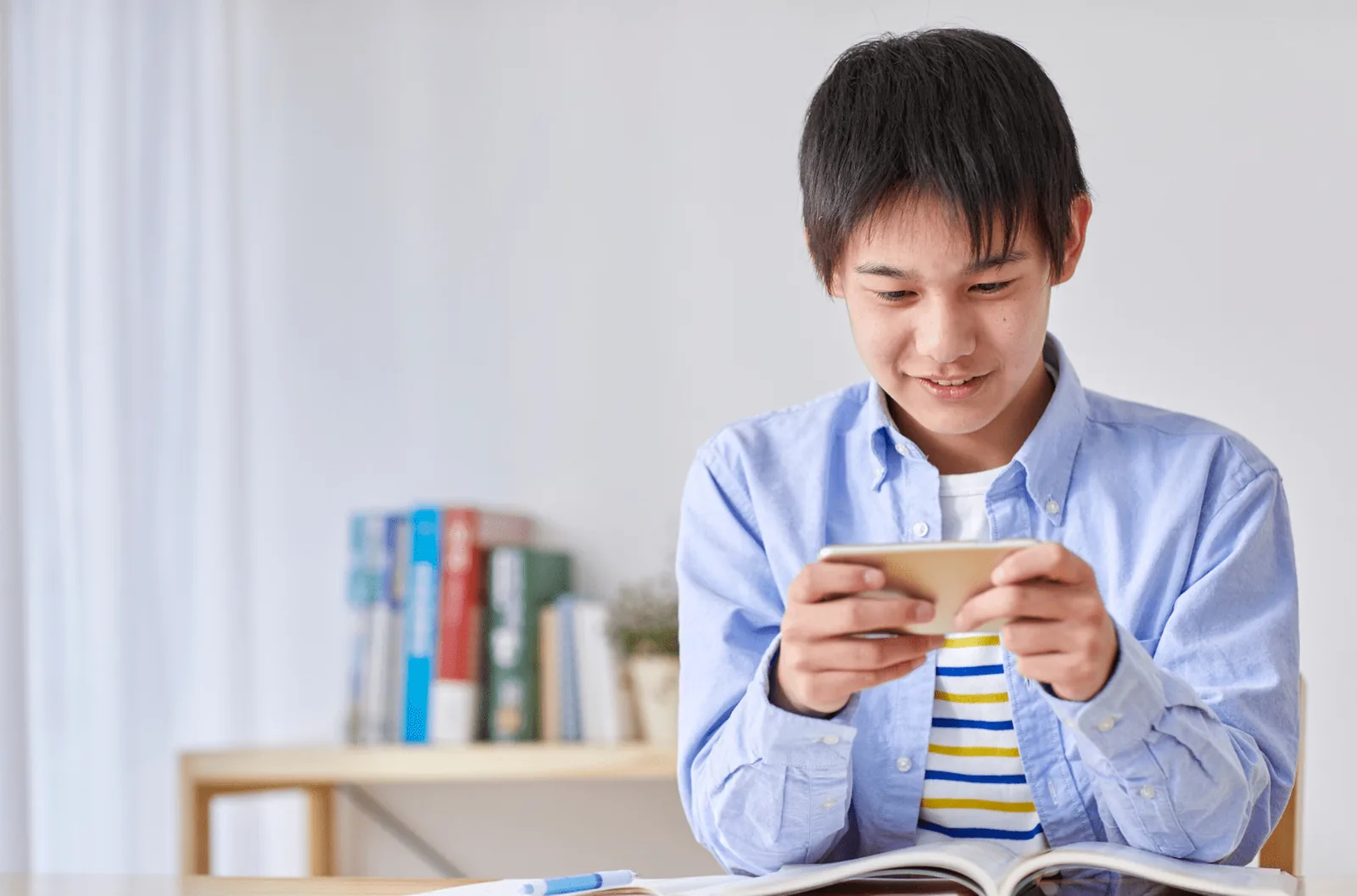 Boy holding a phone at a desk with school materials.