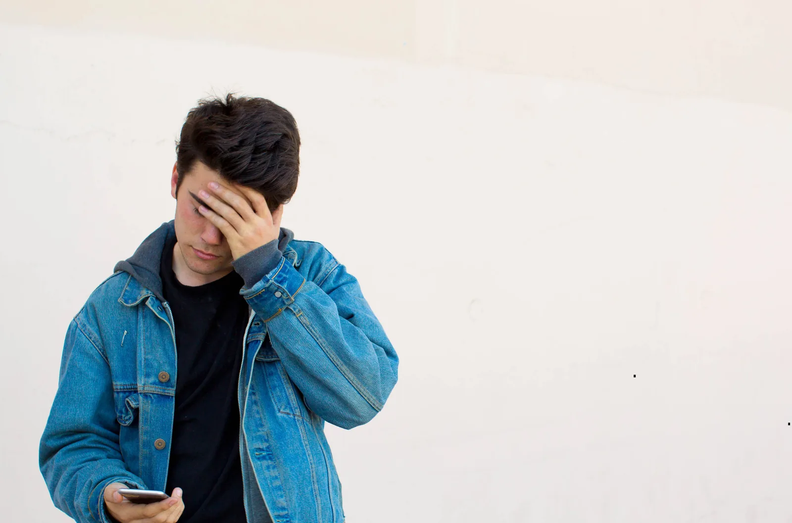 Young person in a blue jacket covering their face with one hand.