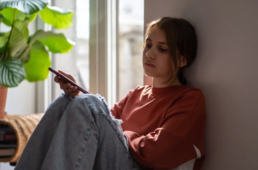Girl sitting by a window looking at her phone.
